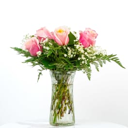 Pink roses with white filler flowers in a clear glass vase