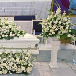 White floral funeral spray arranged around a white casket
