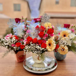 Three colorful flower arrangements in small vases on a table