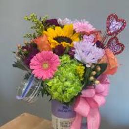 Colorful bouquet with a sunflower, gerbera daisies, and a pink ribbon in a purple vase