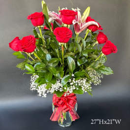 Red roses and lilies arranged in a clear vase with a red ribbon.