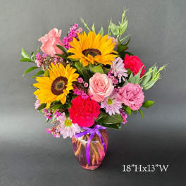 Mixed bouquet with sunflowers, roses, carnations, and daisies in a glass vase