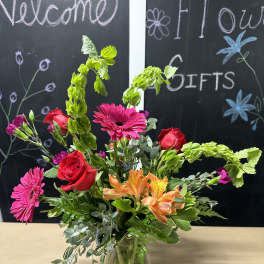 Mixed bouquet with roses, gerbera daisies, and orange alstroemeria in a glass vase