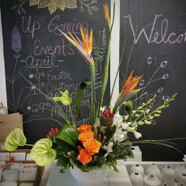 Tropical floral arrangement with orange roses and bird-of-paradise in a white vase
