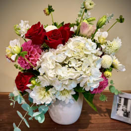 Mixed arrangement of red roses, white hydrangeas, and pink dahlias in a white vase