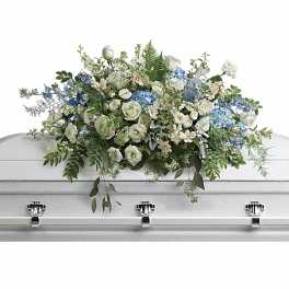 Long spray of white and light blue flowers arranged on top of a white casket