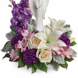 Sympathy arrangement of white lilies, cream roses, and purple flowers with a white angel figurine.