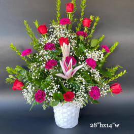 Tall bouquet of red roses, pink carnations, and white lilies in a white basket