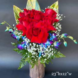 Red roses with blue orchids in a tall vase arrangement
