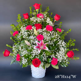 Tall bouquet of red roses, pink carnations, and a pink lily in a white basket vase