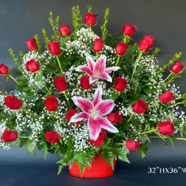 Large arrangement of red roses and pink lilies in a red container