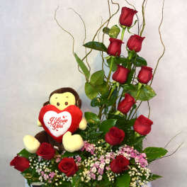 Red roses arranged with a plush teddy bear holding a heart