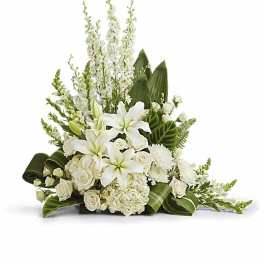 Asymmetrical white arrangement with lilies, roses, and other blooms in a low container with bold green leaves.