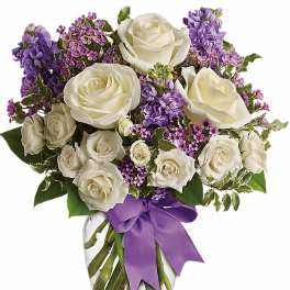 Round glass vase of white roses and lavender flowers with a purple bow