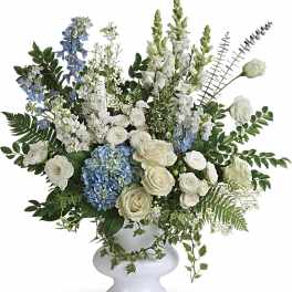 Tall white and blue arrangement of roses, hydrangeas, and snapdragons in a white pedestal vase