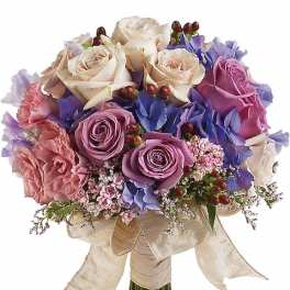 Hand-tied bouquet of ivory and lavender roses with pink blooms and blue flowers wrapped in an ivory ribbon