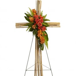 Tall bamboo cross on stand with orange roses and orchids accented by lush green foliage