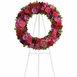 Circular wreath of red and pink flowers displayed on a white metal easel