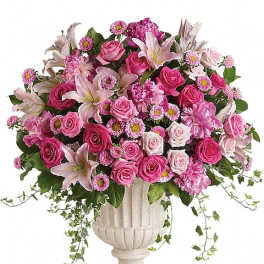 Large pink and white arrangement of roses and lilies in a white urn-style vase with trailing ivy