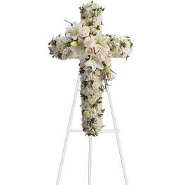 Standing cross-shaped sympathy arrangement of white flowers with white lilies and peach roses on a white easel