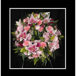 Pink lilies and carnations arranged in a wreath on a black background