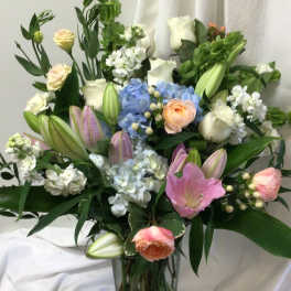 Mixed bouquet of lilies, roses, hydrangeas, and white blooms in a glass vase