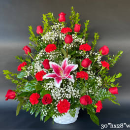Red roses and carnations with a pink lily in a white basket