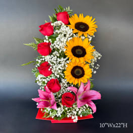 Tall arrangement of red roses, sunflowers, and pink lilies in a red container