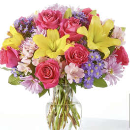 Bouquet of pink roses, yellow lilies, and purple daisies in a glass vase