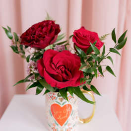 Red roses arranged in a decorative mug with a heart design