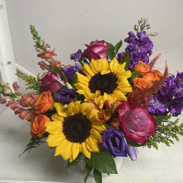 Colorful bouquet with sunflowers, roses, and purple blooms in a white vase