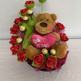Teddy bear surrounded by red roses and gold-wrapped chocolates