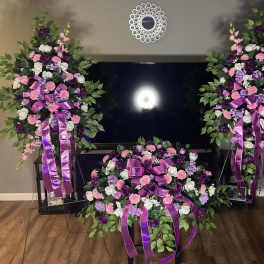 Three purple, pink, and white floral sprays with ribbon accents arranged around a TV.