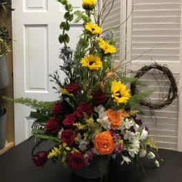 Tall mixed flower arrangement with sunflowers, roses, and white blooms in a vase