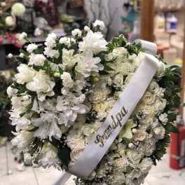 White floral funeral wreath with a white ribbon on an easel