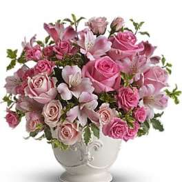 Pink roses and lilies arranged in a white pedestal vase