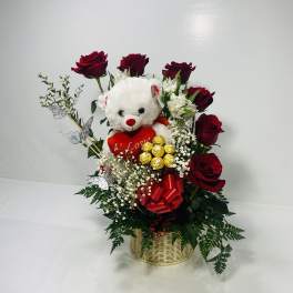 Basket arrangement with red roses, a teddy bear, and chocolates