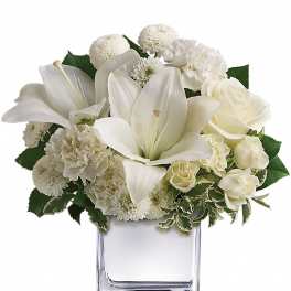 Compact white flower arrangement with lilies, roses, and carnations in a clear glass cube vase