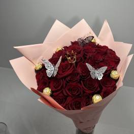 Bouquet of red roses wrapped in pale pink paper with chocolate candies and butterfly picks
