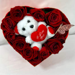 Heart-shaped box of red roses with a small teddy bear holding a heart