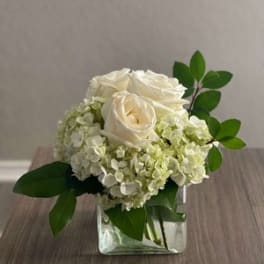 White roses and pale hydrangeas in a clear square vase