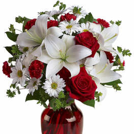 Arrangement of white lilies, red roses, red carnations and white daisies in a red glass vase