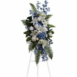 Tall standing spray of white lilies and roses with blue hydrangea and blue delphinium on a white easel