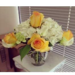 Round vase arrangement with yellow roses, white hydrangeas, and white calla lilies