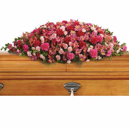 Pink and red casket spray of carnations and mixed flowers on a wooden casket.