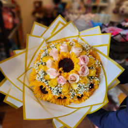 Bouquet of sunflowers and pale pink roses wrapped in white and yellow paper