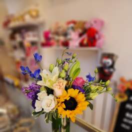Mixed bouquet in a clear glass vase with a sunflower, roses, and lilies
