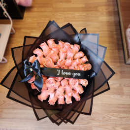 Bouquet of peach-pink roses wrapped in black paper with a ribbon