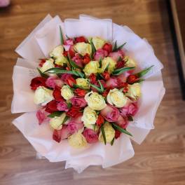 Bouquet of pink, red, and yellow roses wrapped in white paper