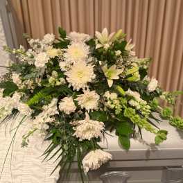 Large white floral spray on a casket with green foliage